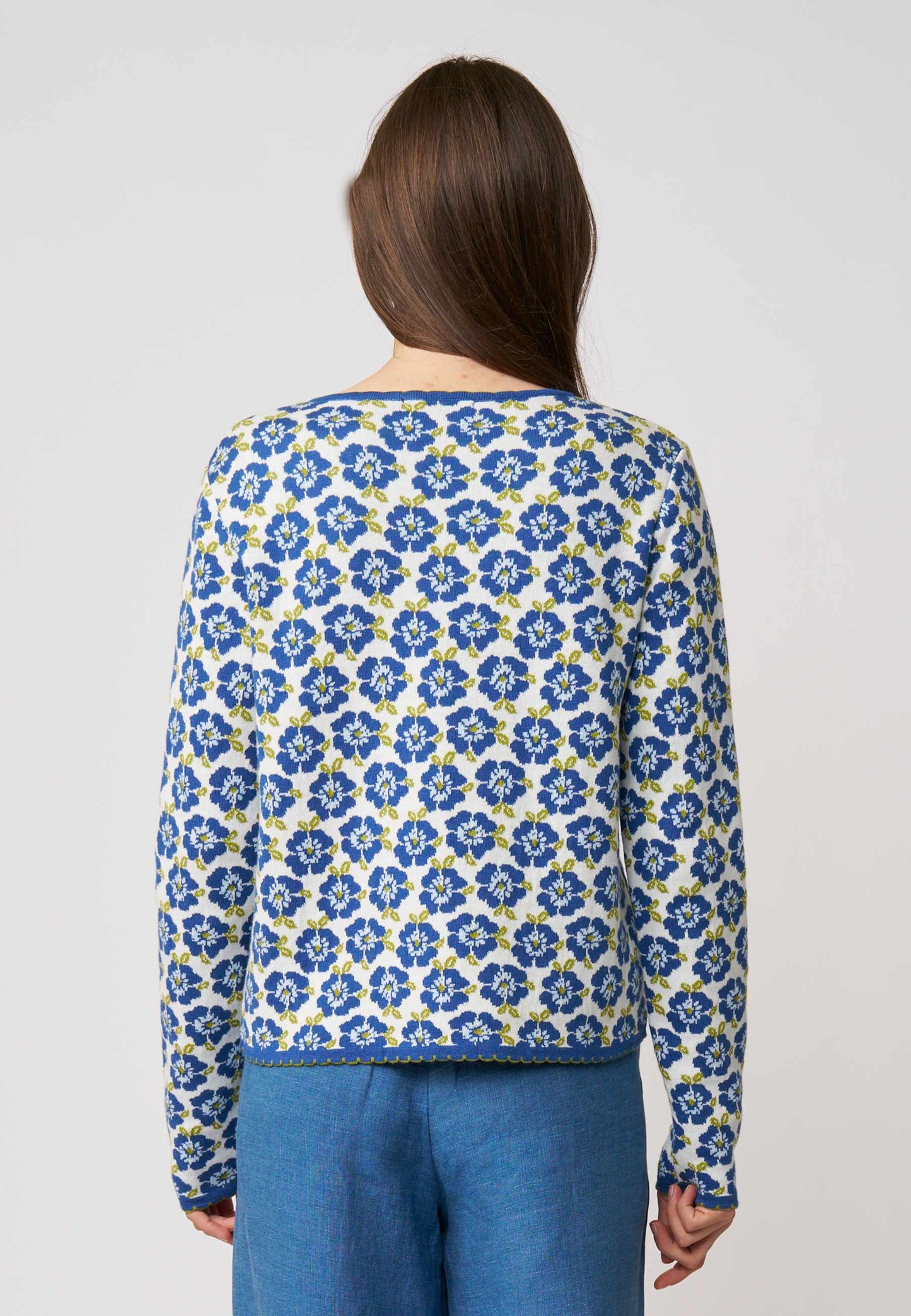 Frau trägt Strickjacke, Modell Juliana, mit blauem Blumenmuster und zierlichem Saum in Naturweiß, Rückansicht