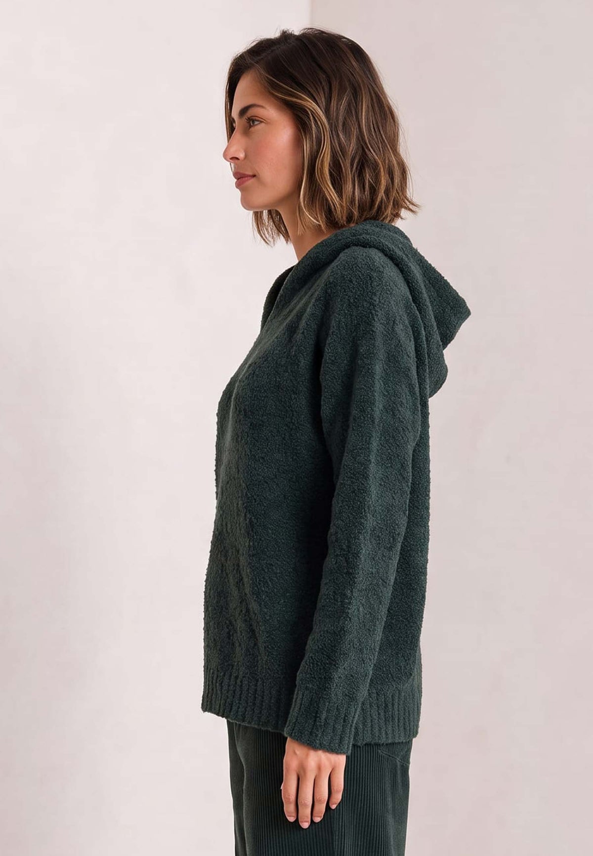 Frau trägt dunkelgrünen Kapuzenpulli, Modell Hedda, im Profil vor hellem Hintergrund